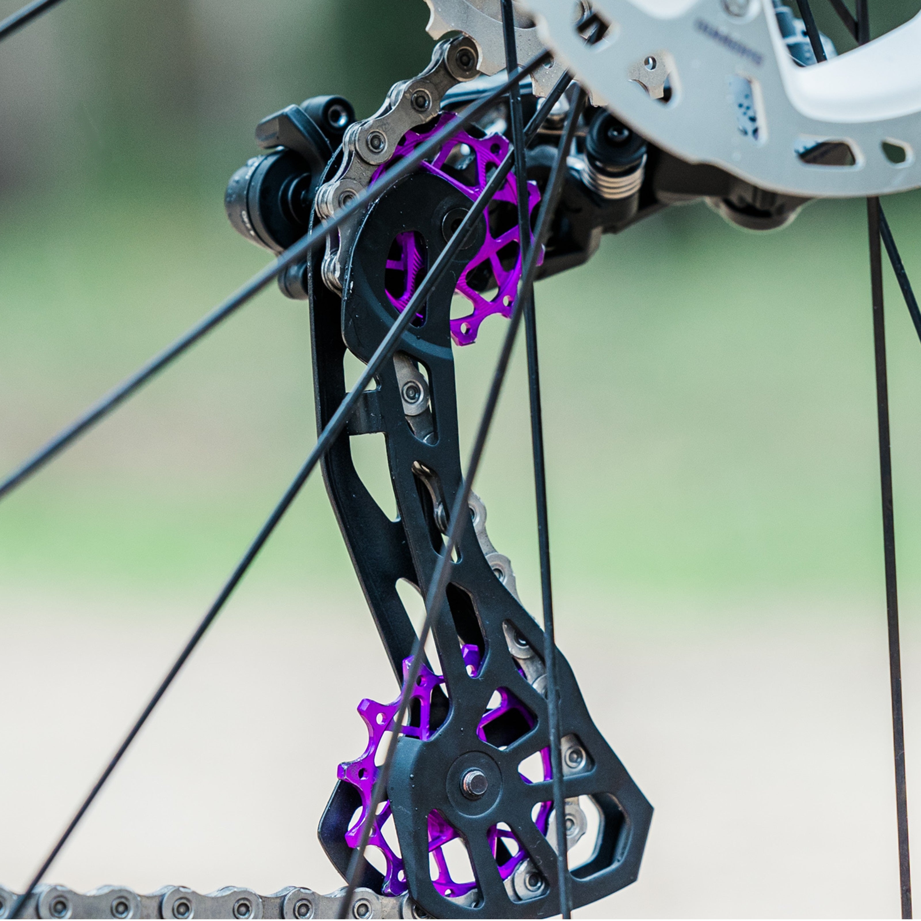 Close-up of colourful purple Garbaruk rear derailleur pulleys for Shimano mounted on a titanium Bossi bike, showcasing CNC-machined detail and precision engineering