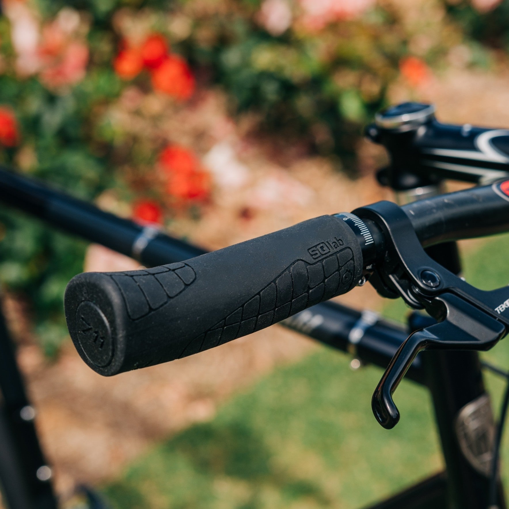 Close up of SQLab 711 grip installed on a flat bar commuter bike, photographed in a rose garden