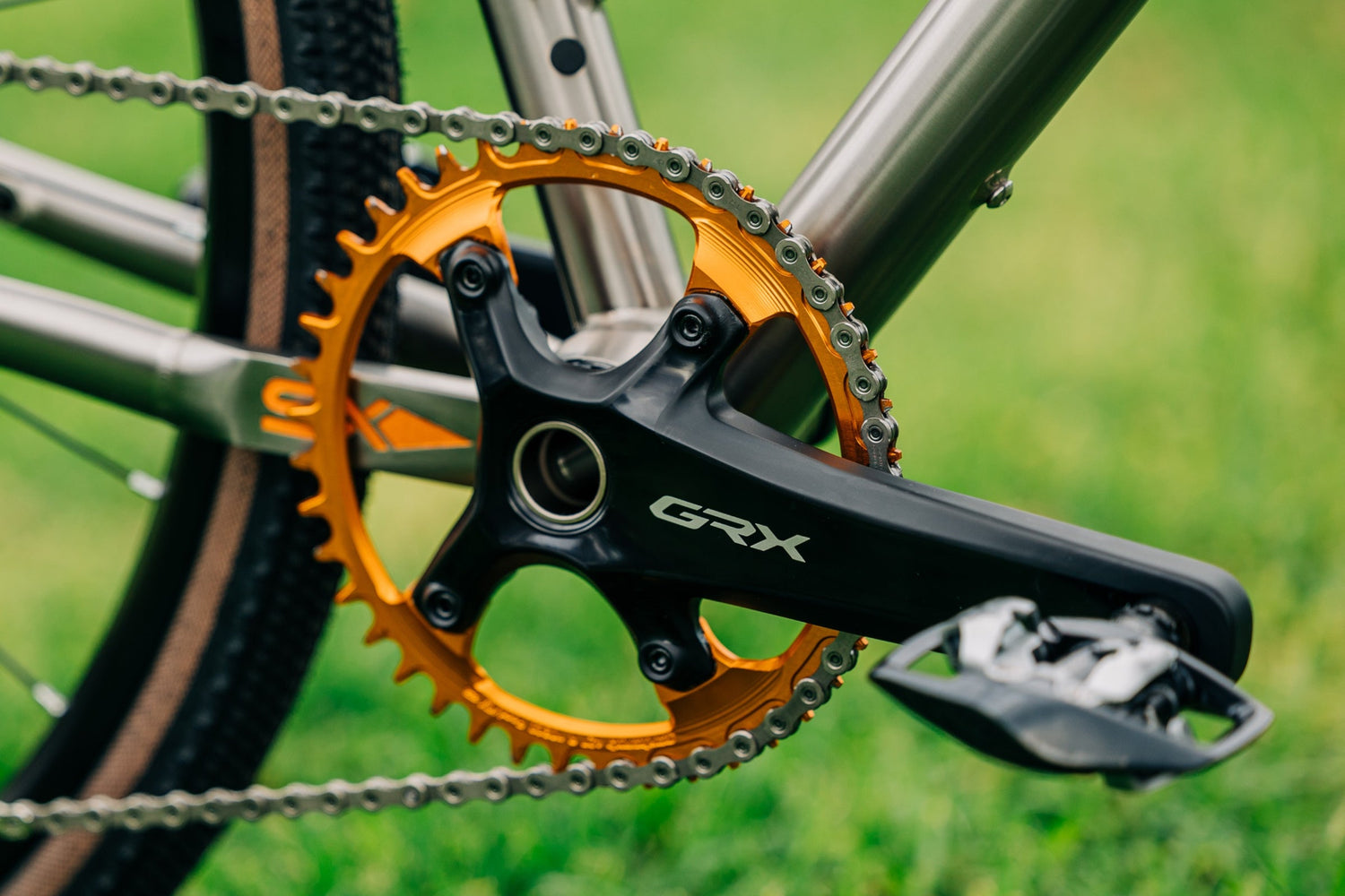 An orange Garbaruk chainring fitted to a Shimano GRX crankset, photographed outside on a grassy lawn