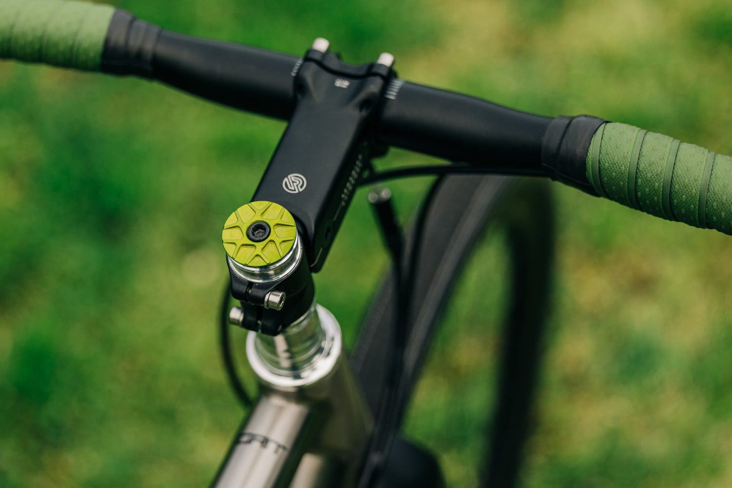 A green Garbaruk top cap fitted to a titanium Bossi Grit, photographed against a green lawn