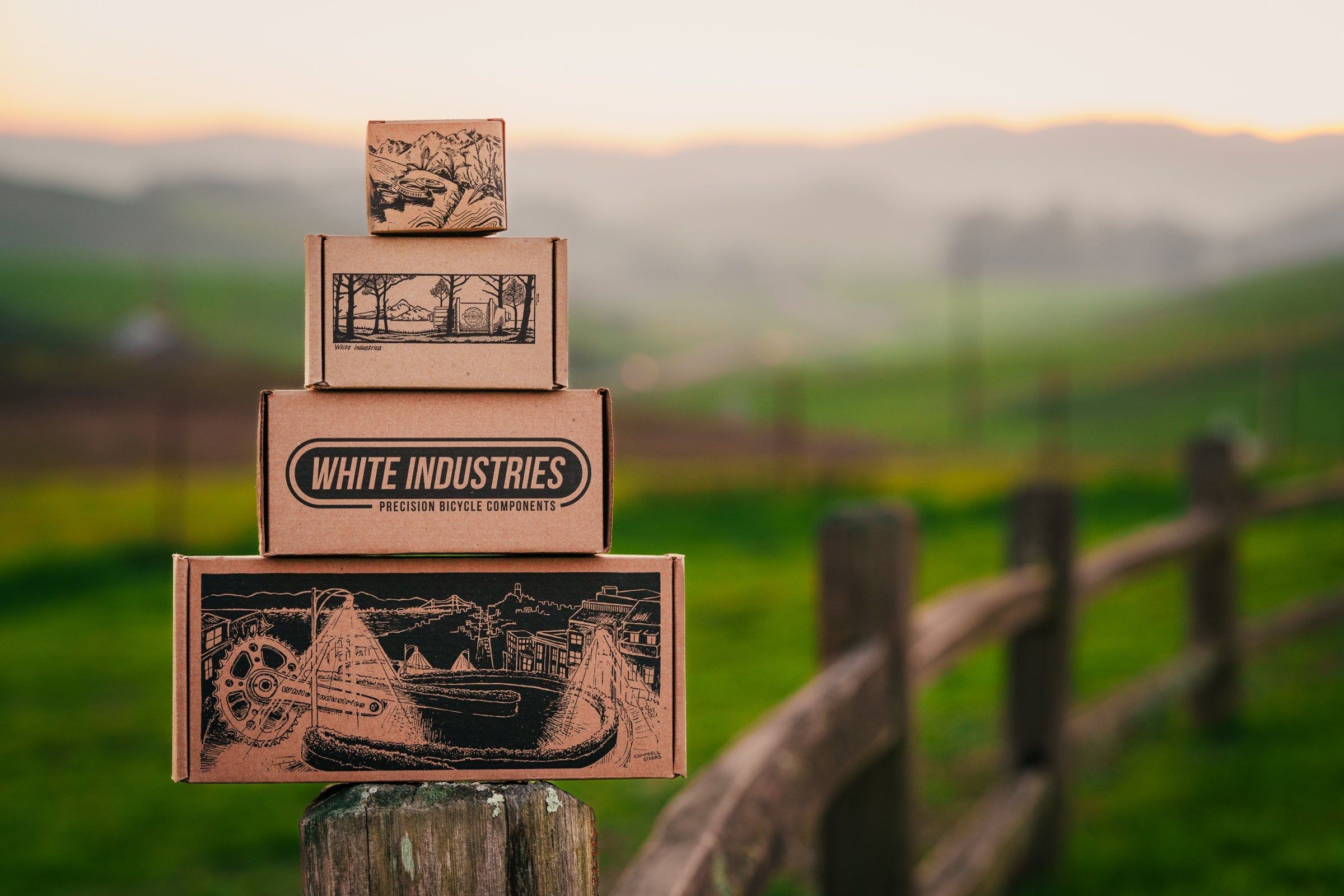Boxes of White Industries bike components, balanced on a fence post