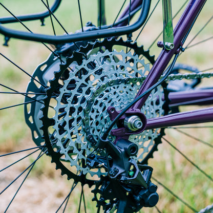 Garbaruk 12sp Shimano Microspline cassette in black, fitted to a purple steel bike, shot outdoors against a grassy background
