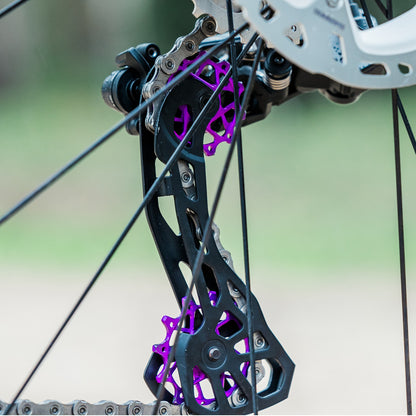 Close-up of colourful purple Garbaruk rear derailleur pulleys for Shimano mounted on a titanium Bossi bike, showcasing CNC-machined detail and precision engineering