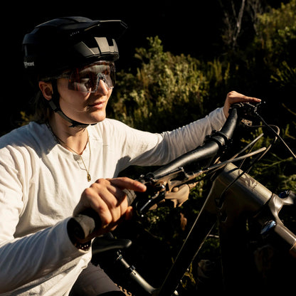A mountain biker using a set of SQLab 70X 2.0 mountain bike grips, pushing a mountain bike up a hill in bright sunlight, dark green foliage in the background